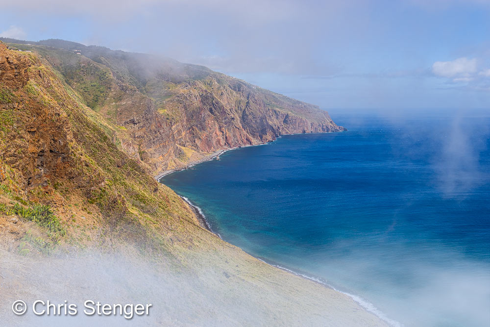 De westkust van Madeira bestaat uit kliffen die steil uit zee omhoog rijzen. Ik maakte de foto met harde wind waardoor de omstandigheden steeds wisselden. Voortdurend trokken flarden mist vanuit zee landinwaarts. Een spectaculait gezicht. 